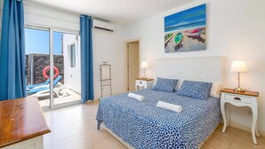 Een slaapkamer met een bed, twee nachtkastjes, een schilderij van boten en uitzicht op een zwembad.