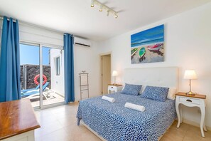 Ein Schlafzimmer mit einem Bett, zwei Nachttischen, einem Bild von Booten und Blick auf einen Poolbereich.