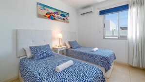 Hotelkamer met twee bedden, een nachtkastje, een lamp, een schilderij, een airconditioning en een raam met gordijnen.