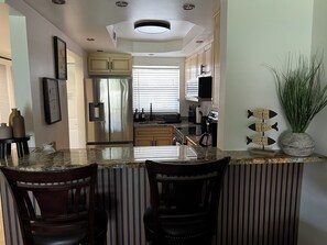 A modern kitchen with a central island, bar seating, and a large window. - Sunsets, sand & Style - Naples Getaway (Naples)
