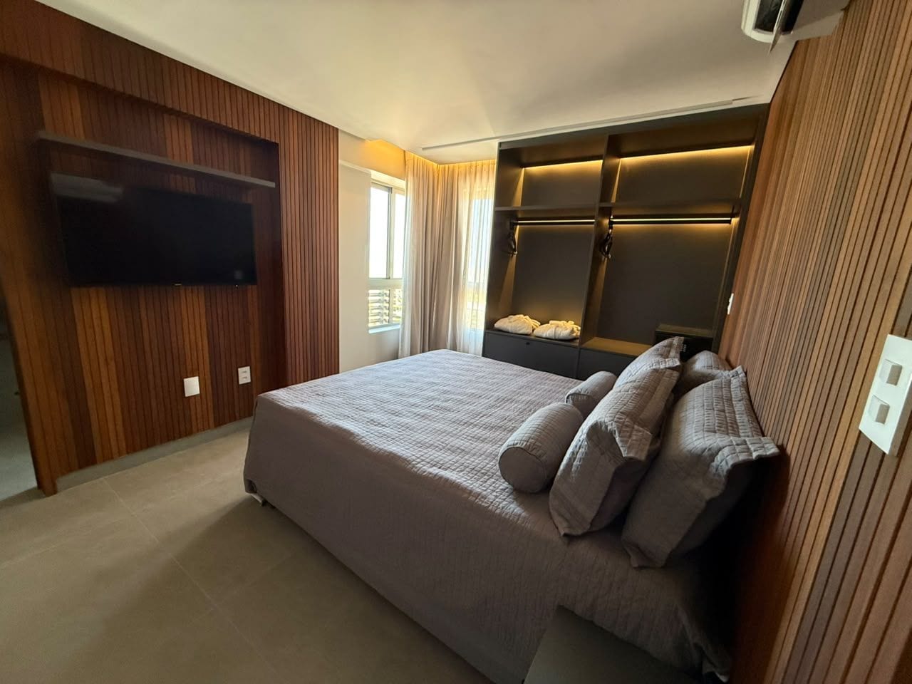 A bedroom with a bed, a flat-screen TV mounted on the wall, and a built-in wardrobe.