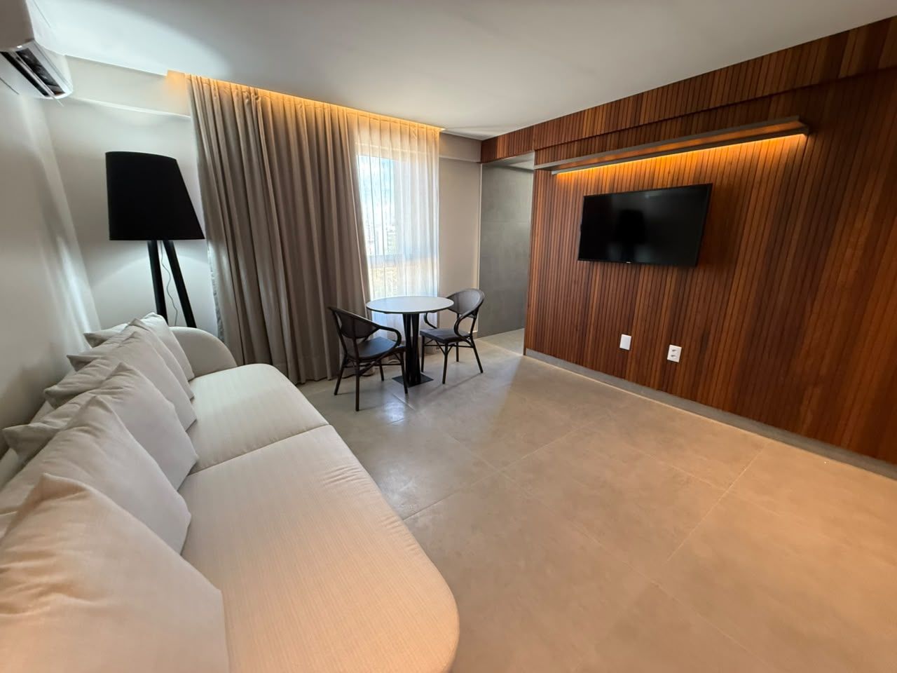 Una sala de estar moderna con un sofá, una mesa de comedor con sillas, un televisor de pantalla plana montado en una pared de madera y una lámpara.