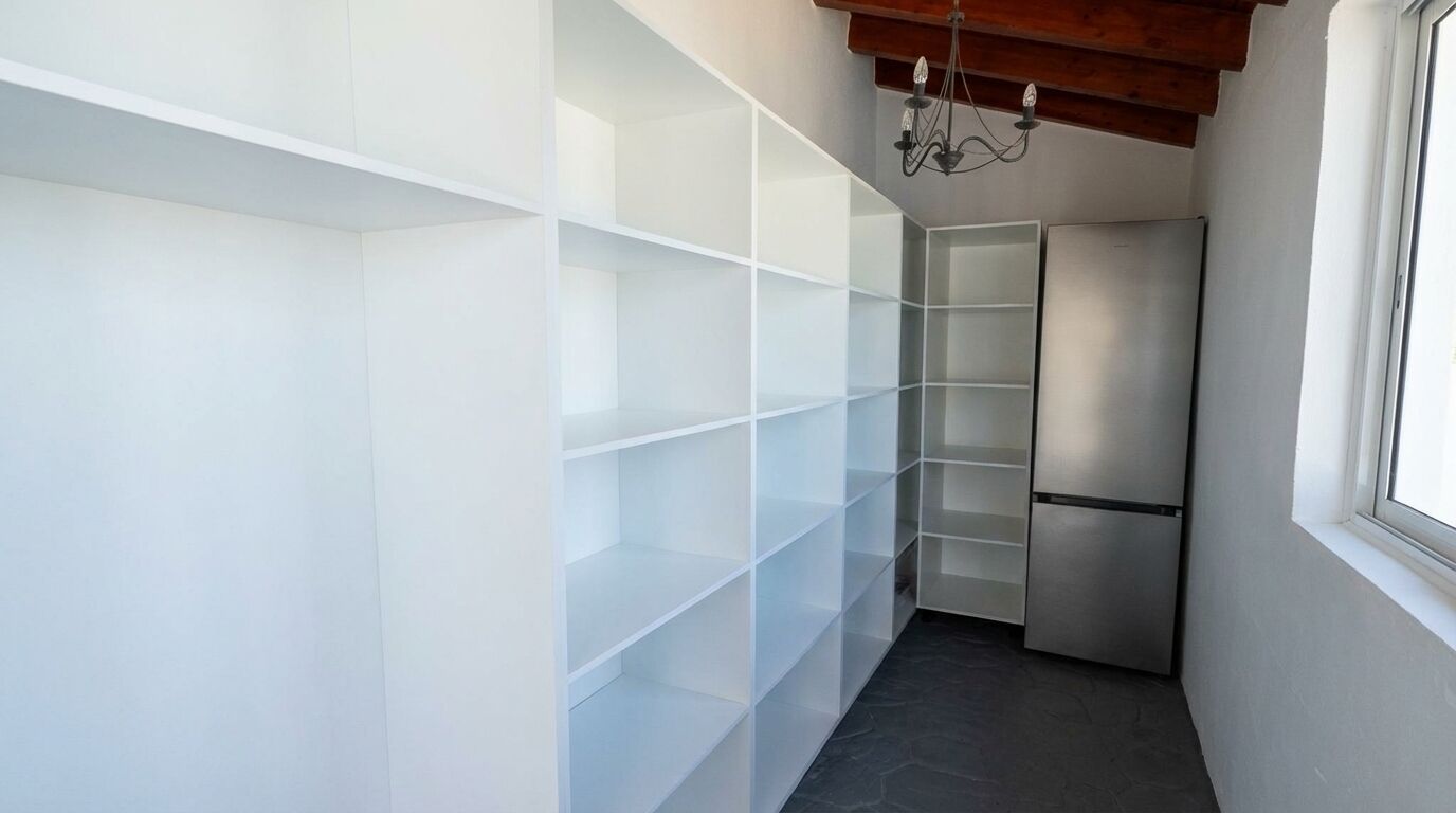 A narrow hallway with white shelving units and a stainless steel refrigerator.