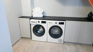 A laundry area with two front-loading washing machines and a stacked pile of white towels on a black countertop. - Exclusive Mountain Villa (Barranco Hondo)