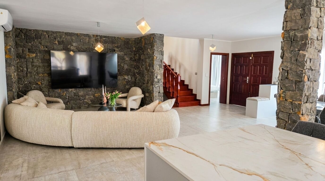 Ein modernes Wohnzimmer mit Steinwand, Flachbildfernseher, beiges Sofa und Marmortisch.