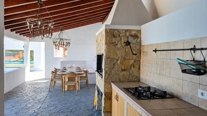 A modern kitchen with a stone wall, a gas stove, and a dining area with a table set for four. - Exclusive Mountain Villa (Barranco Hondo)