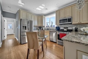 A modern kitchen with stainless steel appliances, a granite countertop, and a dining area with a glass table. - Enjoyable 3-bedroom apartment with AC in vibrant Somerville (Somerville)