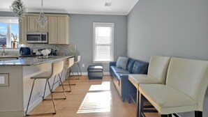 Een moderne keuken met een bar, een zithoek met een bank en stoelen, en een groot raam dat zorgt voor veel daglicht.