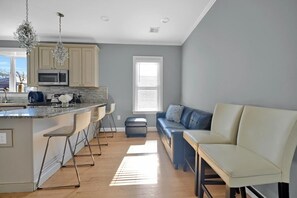 A modern kitchen with a bar area, a seating area with a sofa and chairs, and a large window providing natural light. - Enjoyable 3-bedroom apartment with AC in vibrant Somerville (Somerville)