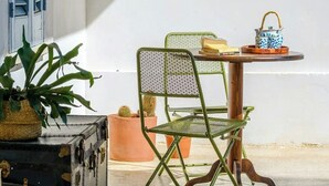 Quarto com uma mesa, uma cadeira, um vaso de planta e uma mala.