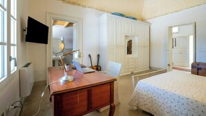 Quarto com escrivaninha de madeira, cama com colcha florida, guarda-roupa e televisão na parede.