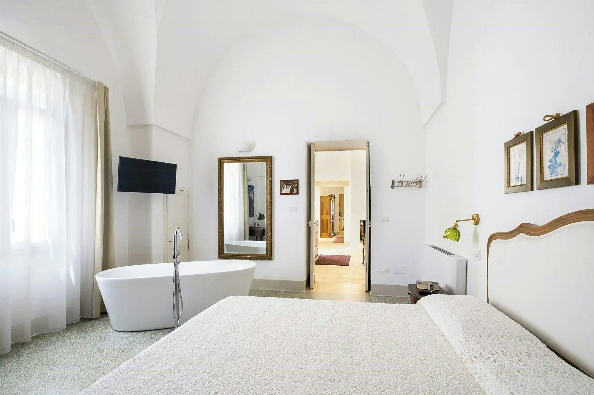 A hotel room with a large bed, a bathtub, a flat-screen TV, and a door leading to another room.