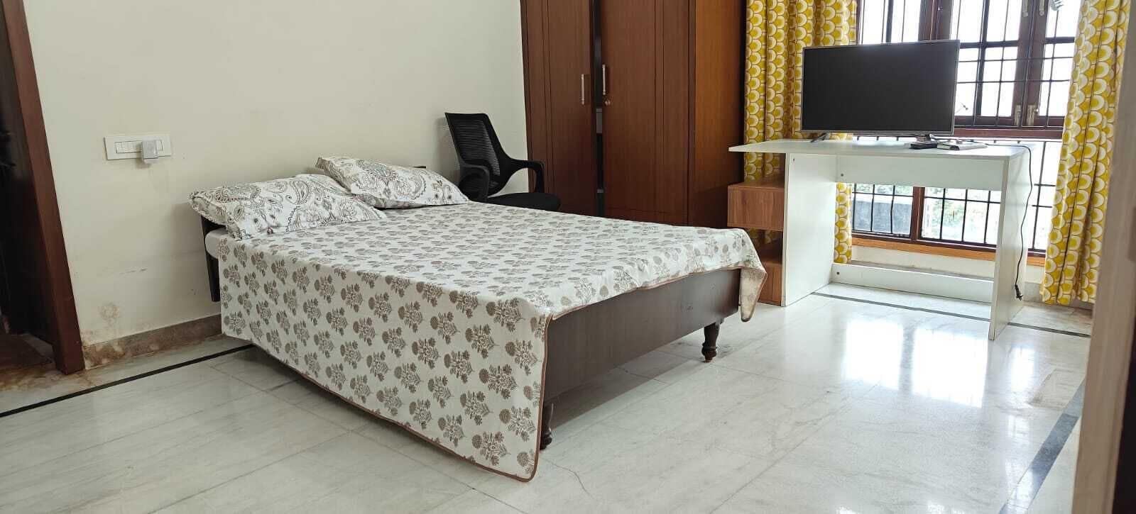 Une chambre à coucher avec un lit, une chaise, un bureau avec une télévision et une fenêtre avec des rideaux.