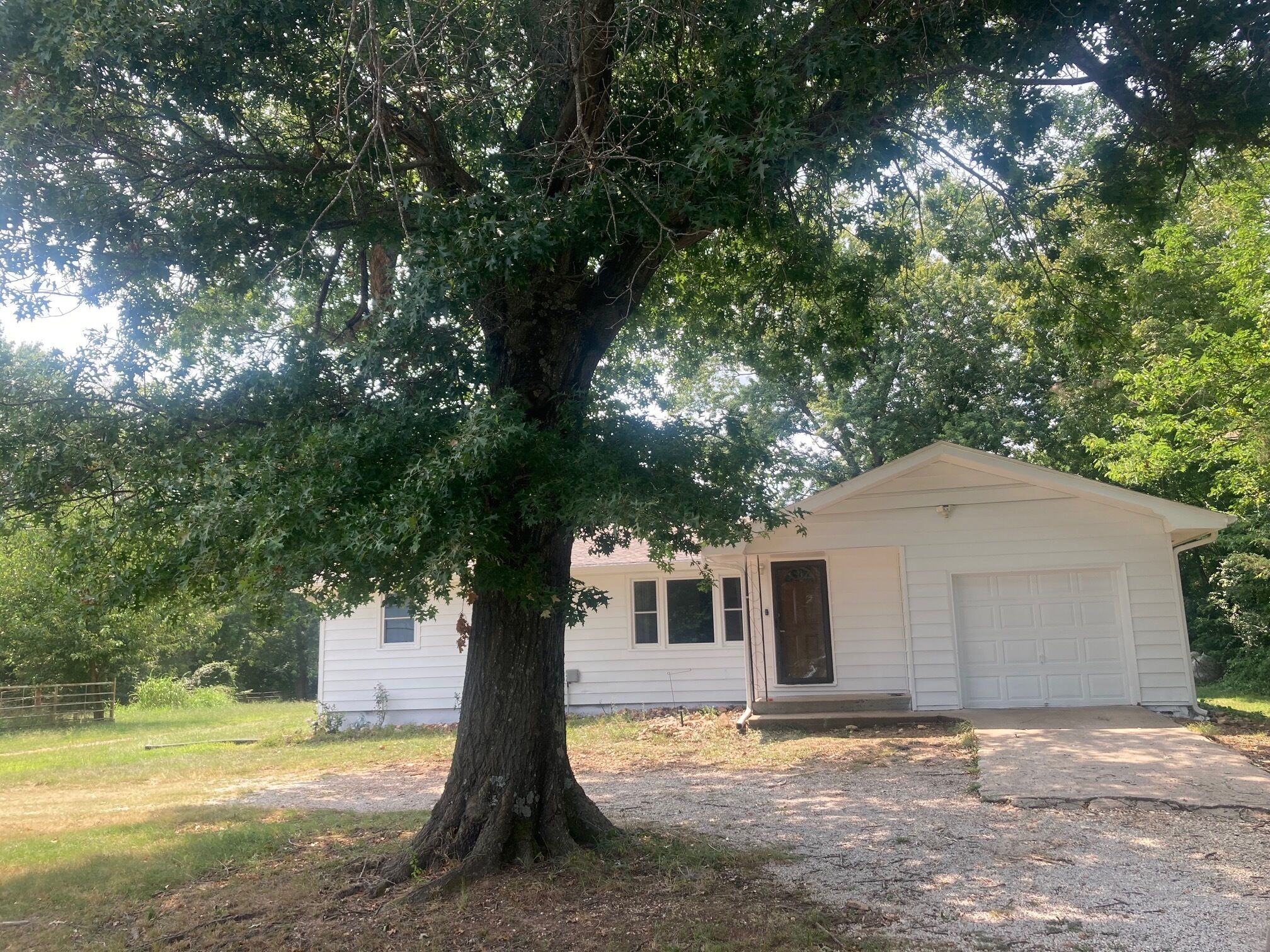 A single-story house with a large tree in front, a garage, and a small porch.