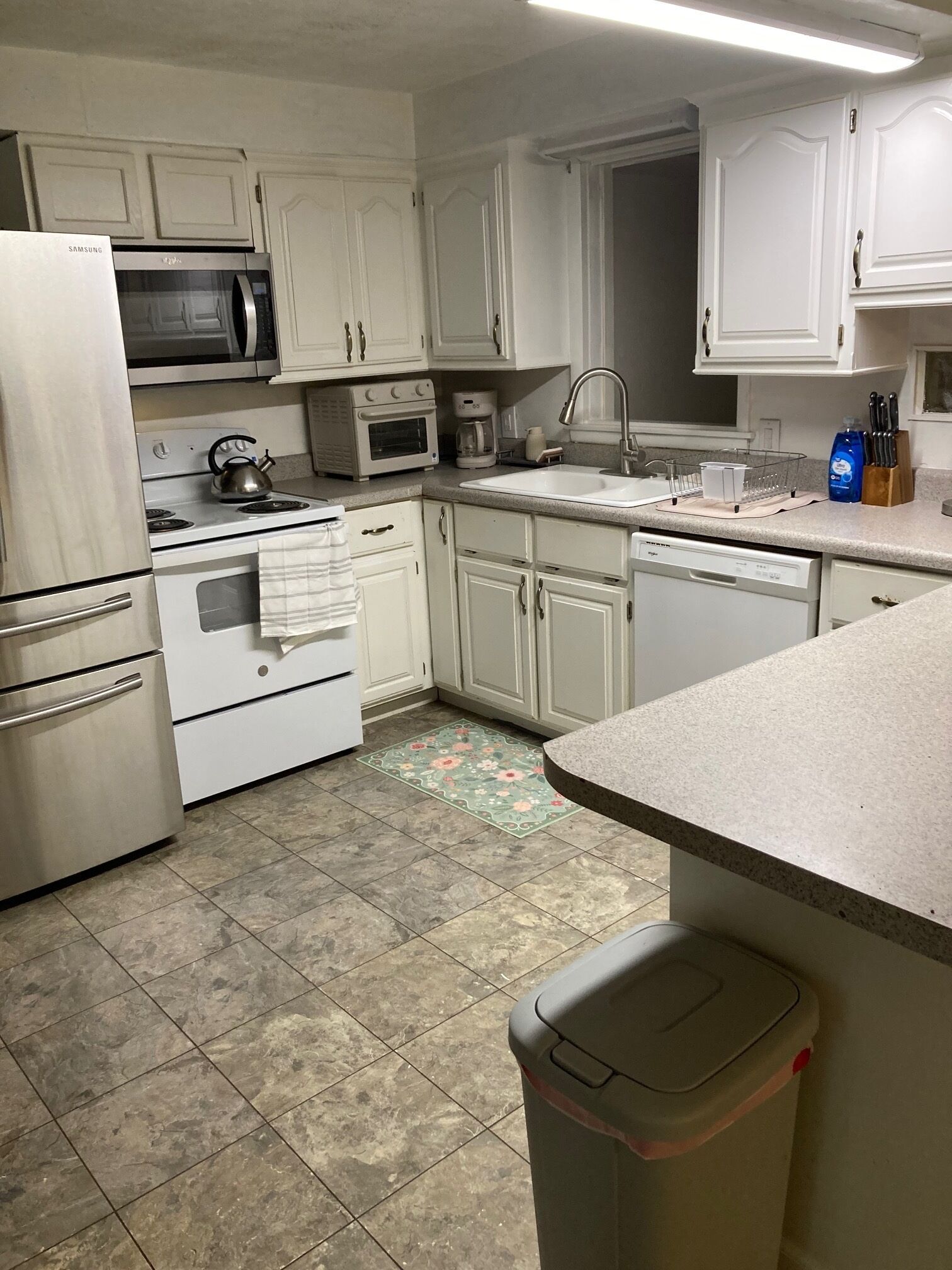 A kitchen with white cabinets, a microwave, stove, oven, sink, and a trash bin.