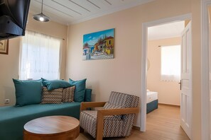 A living room with a sofa, a patterned armchair, a wooden coffee table, and a painting on the wall. - Apartment 'Dervisia Stone Houses 1' with Lake View, Wi-Fi and Air Conditioning (Lazarata)