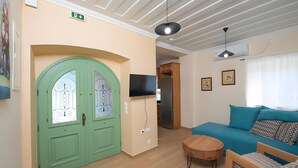 Ein Zimmer mit grüner Tür, einem Flachbildfernseher, einem Sofa und einem kleinen Tisch.
