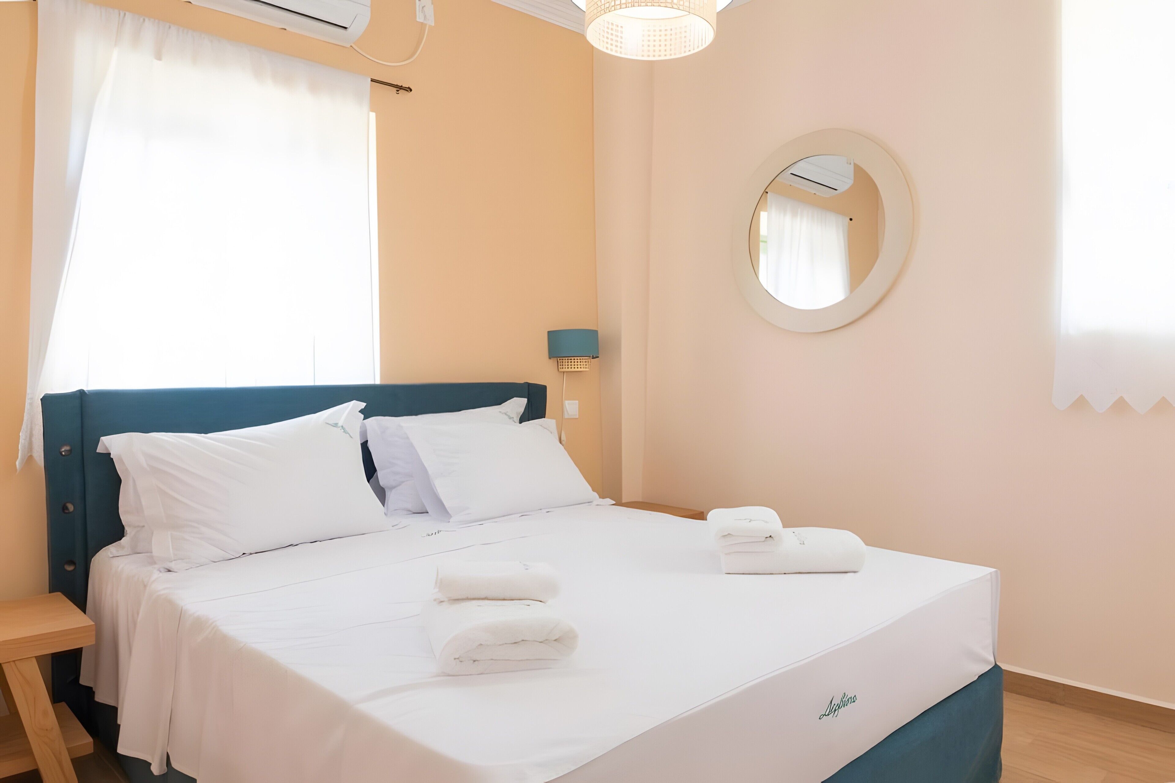 Quarto de hotel com cama, mesa de cabeceira, luminária, espelho e janela com cortinas.