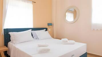 Quarto de hotel com cama, mesa de cabeceira, luminária, espelho e janela com cortinas.