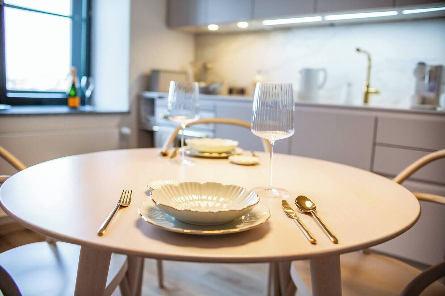 Een ronde eettafel met een witte tafelkleed, een wijnglas, een bord en bestek.