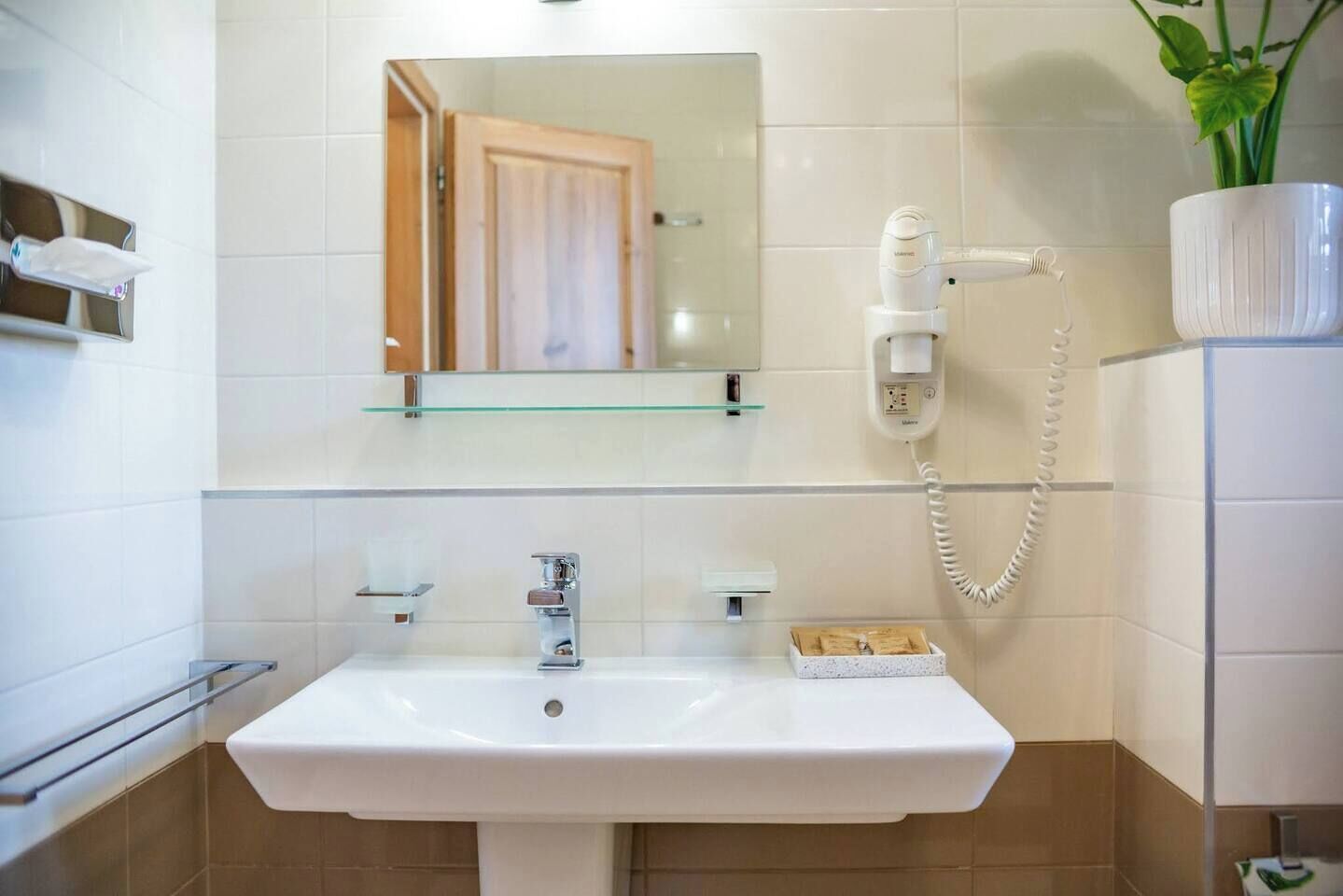 Ein Badezimmer mit einem weißen Waschbecken, einer Glasablage darüber, einem Spiegel, einem Handtuchhalter und einem Telefon.