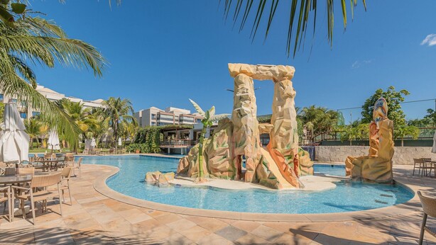 Ein Pool mit einer Felsformation im Zentrum, Sitzgelegenheiten im Freien und Palmen.