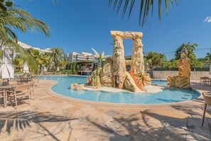 A pool with a rock formation centerpiece, outdoor seating, and palm trees. - Wai Wai #a303 Sea View By Carpediem (Caucaia)