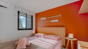 Ein Schlafzimmer mit Bett, Kissen, einem Nachttisch, einer Lampe und einem Fenster mit Aussicht.