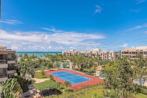 Un complex turístic amb una pista de tennis, palmeres i vista a l'oceà.