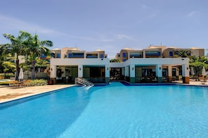Un hotel modern amb piscina central, diversos balcons i palmeres.