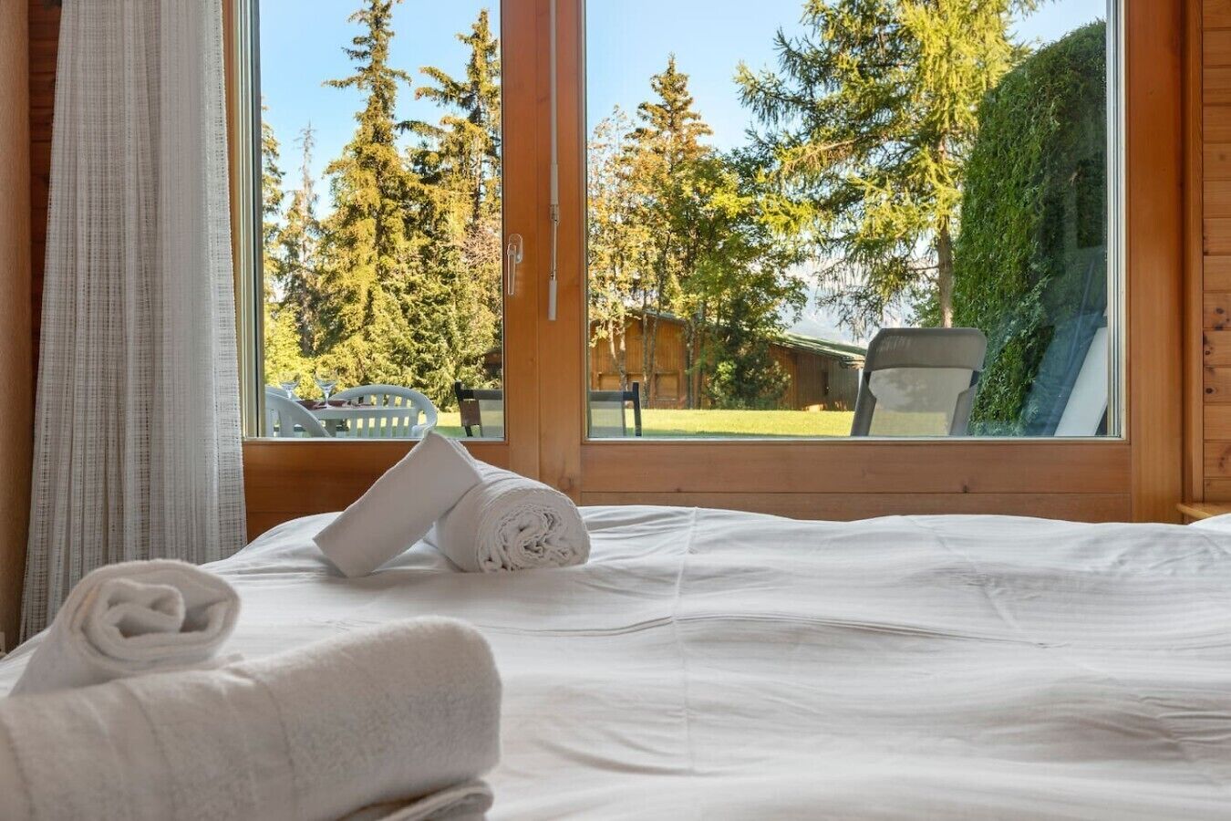 Habitación de hotel con cama, ventana que da a vistas de árboles y un edificio, y una toalla sobre la cama.