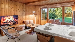 Ein Holzinnenraum mit einem Bett, einem Fernseher, der ein Feuer zeigt, einem Sessel und einem Tisch.