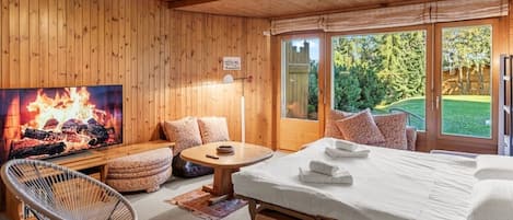 Un interior de madera con una cama, un televisor mostrando un fuego, una silla y una mesa.