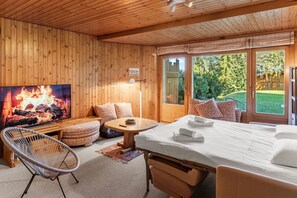 Ein Holzinnenraum mit einem Bett, einem Fernseher, der ein Feuer zeigt, einem Sessel und einem Tisch.