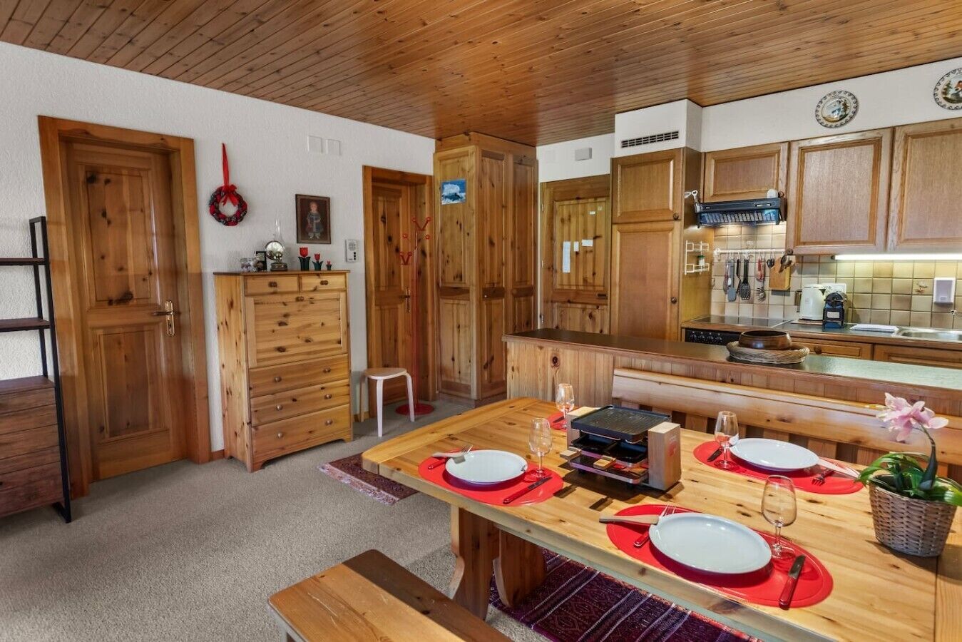 Un intérieur en bois comprenant une table à manger pour quatre personnes, une cuisine avec des placards en bois et un petit tabouret.