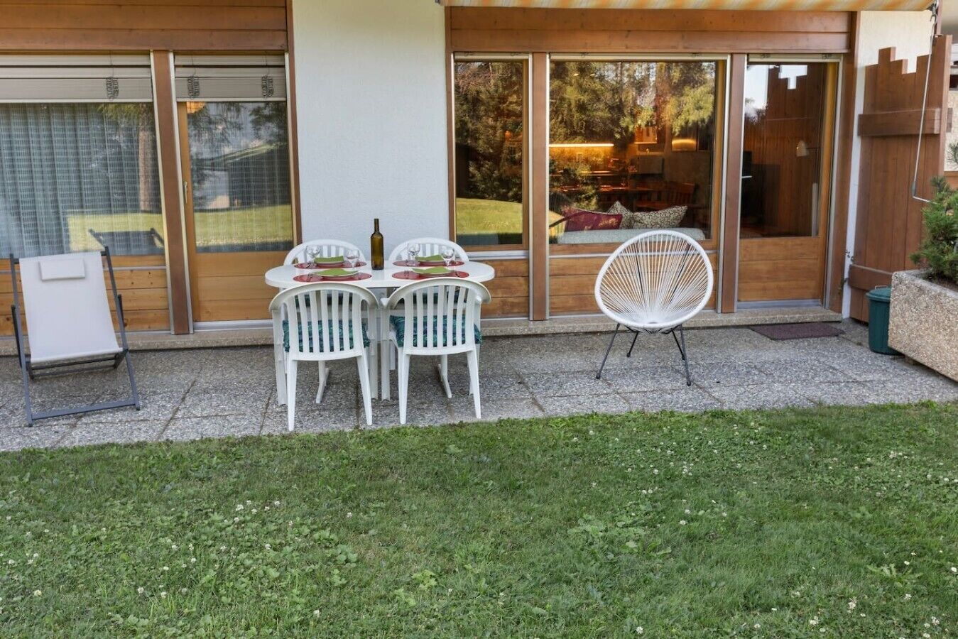 Eine Terrasse mit Tisch für vier Personen, umgeben von weißen Stühlen, und ein einzelner Stuhl außerhalb der Terrasse.