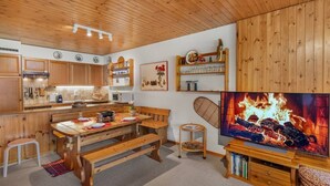 Eine gemütliche Küche mit Holzschränken, einem Esstisch mit Bänken und einem Kamin mit Fernseher.