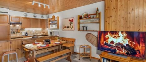A cozy kitchen with wooden cabinets, a dining table with benches, and a fireplace with a TV.