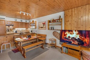 Eine gemütliche Küche mit Holzschränken, einem Esstisch mit Bänken und einem Kamin mit Fernseher.