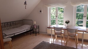 Et værelse med en seng, et bord med stole, et vindue med udsigt til grøn natur og en radiator.