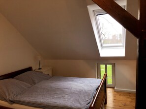 Un dormitorio con techo inclinado, tragaluz, cama con ropa de cama a rayas y mesita de noche con lámpara.