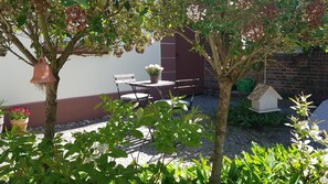 Un patio con mesa y sillas, rodeado de macetas con plantas y un comedero para pájaros.