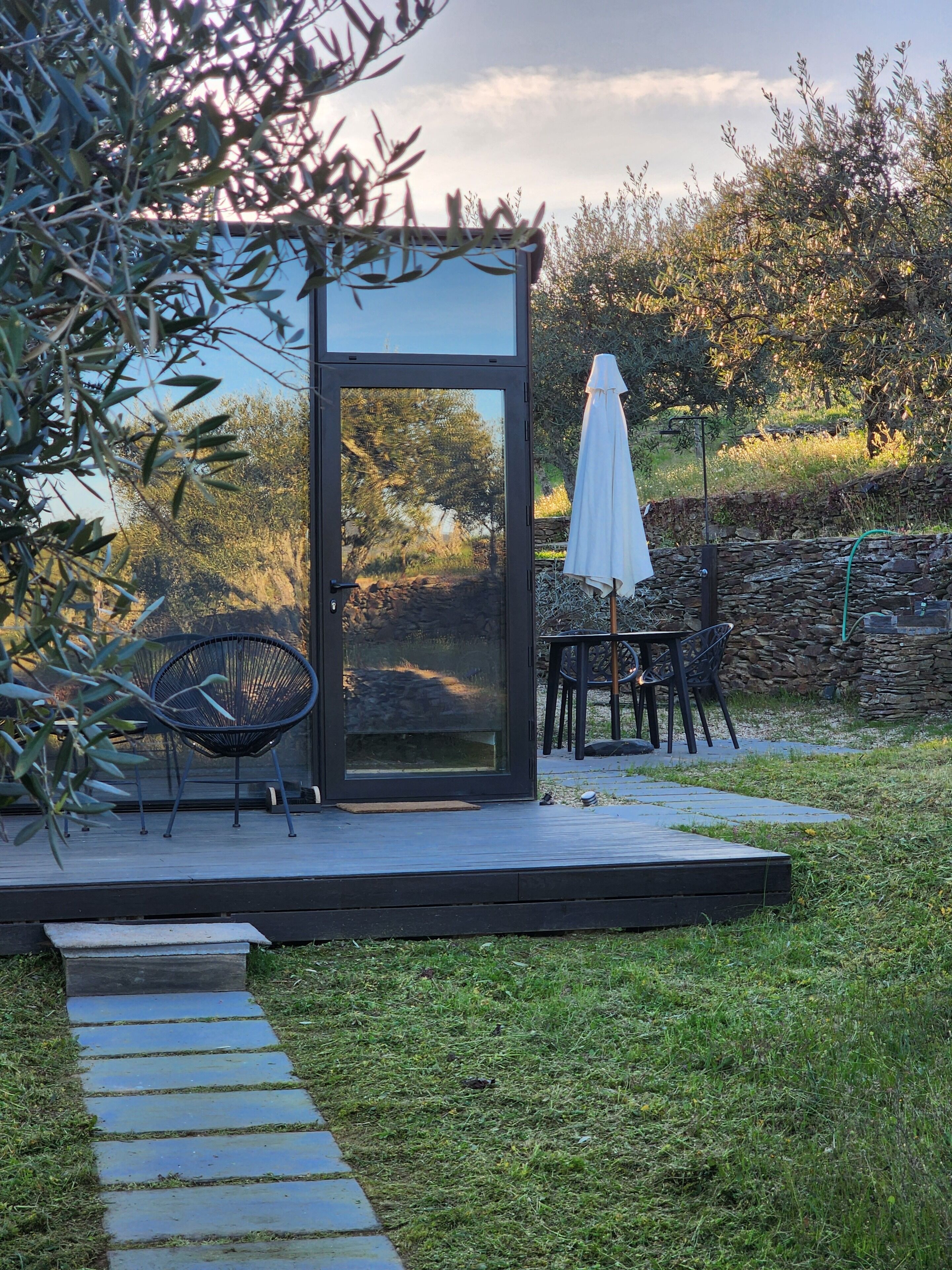 A modern outdoor seating area with a glass enclosure, a stone wall, and a grassy lawn.
