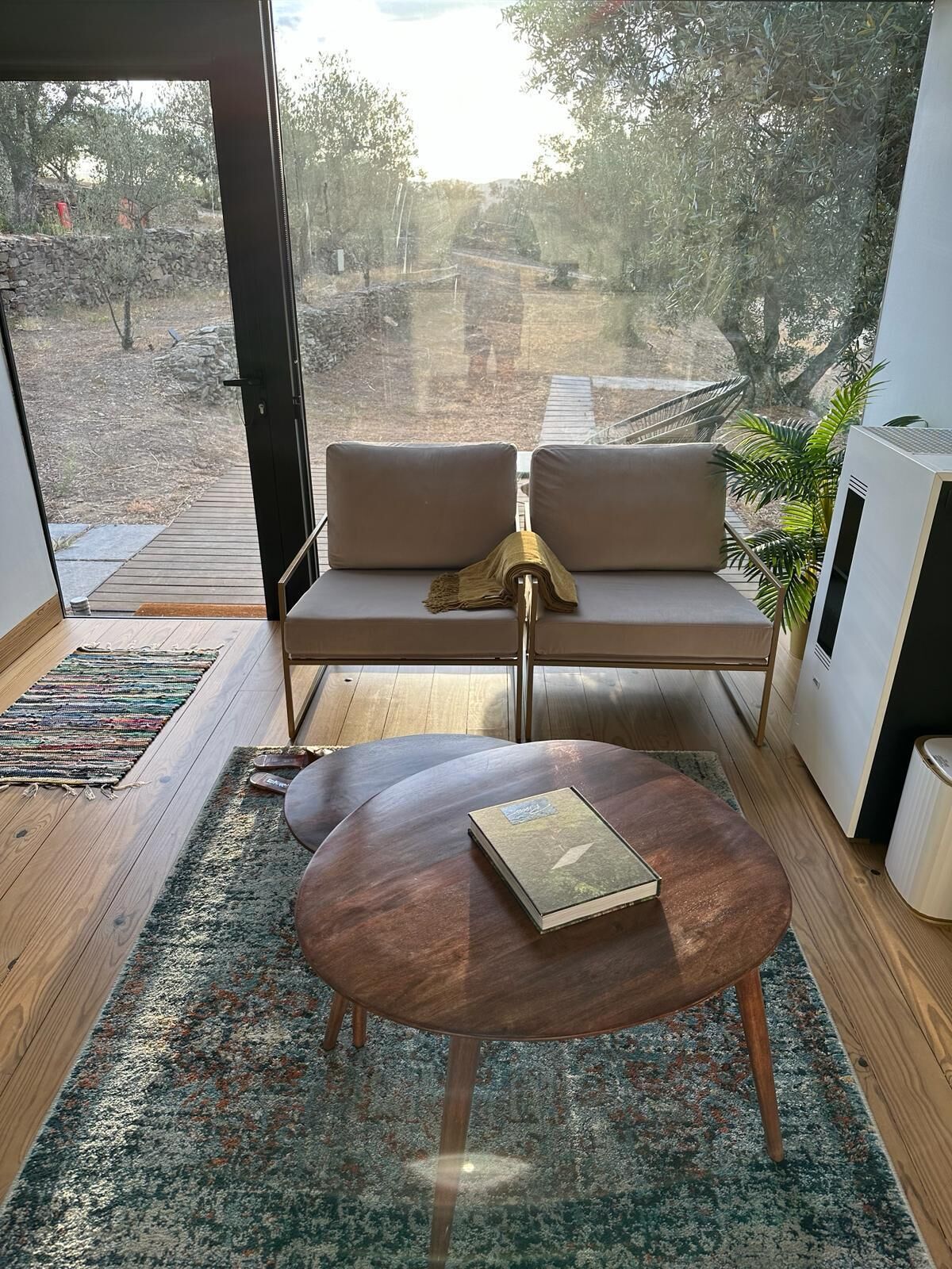 A modern living room with a sofa, a coffee table, and a view of a garden through large windows.