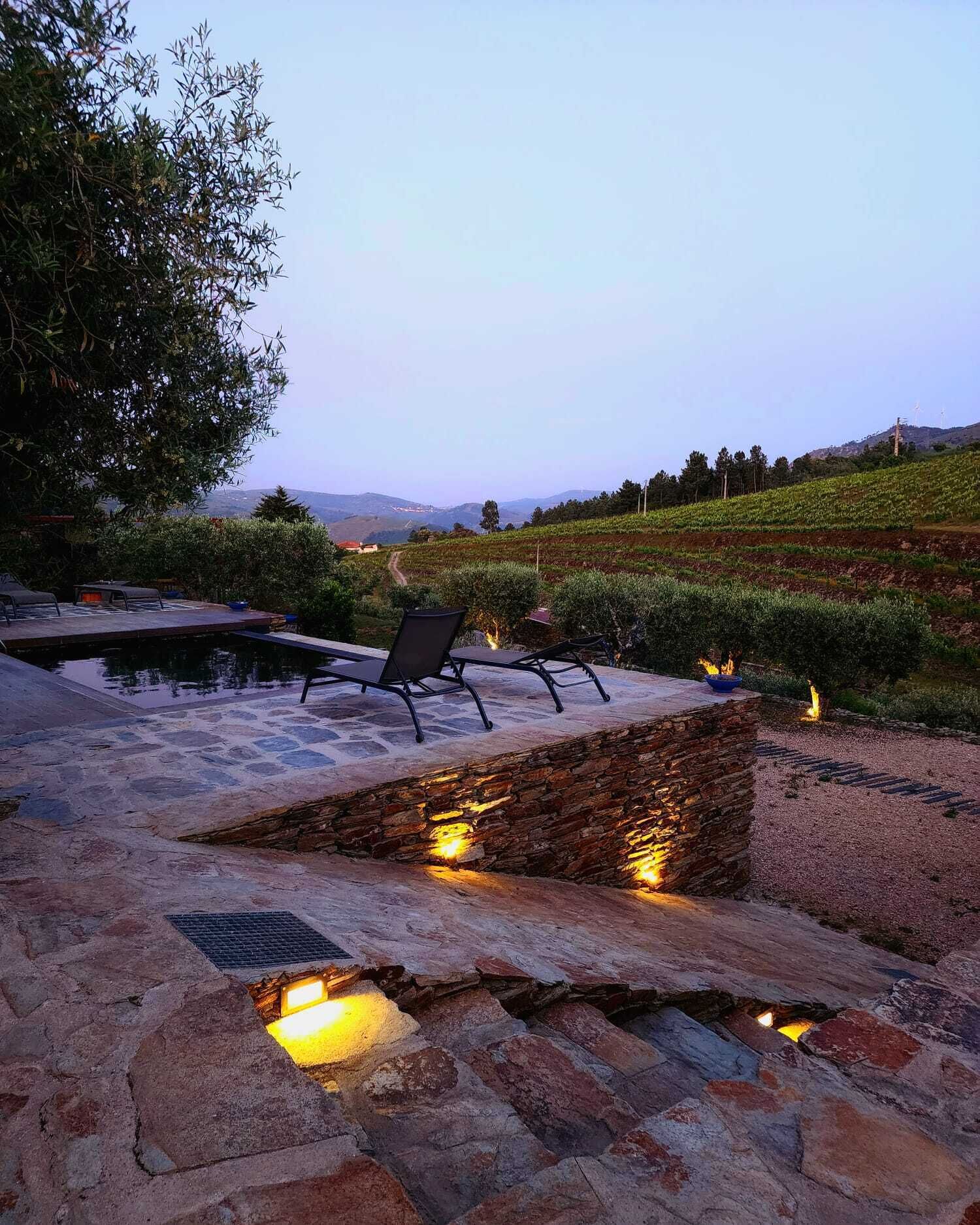 An outdoor seating area with stone flooring and a pool, overlooking a vineyard.