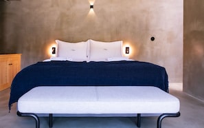 A bed with a dark blue cover, white pillows, and a white bench in front.