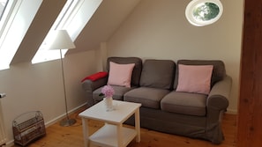 A cozy living room with a brown sofa, a white coffee table, and a floor lamp. - Apartment 'Ferienwohnung Herzmuschel' with Wi-Fi (Jade)