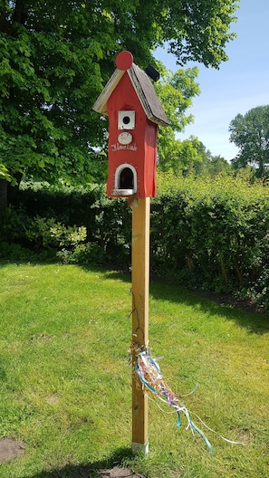 A wooden birdhouse with a red roof and a small entrance, attached to a wooden post with colorful ribbons. - Apartment 'Ferienwohnung Herzmuschel' with Wi-Fi (Jade)