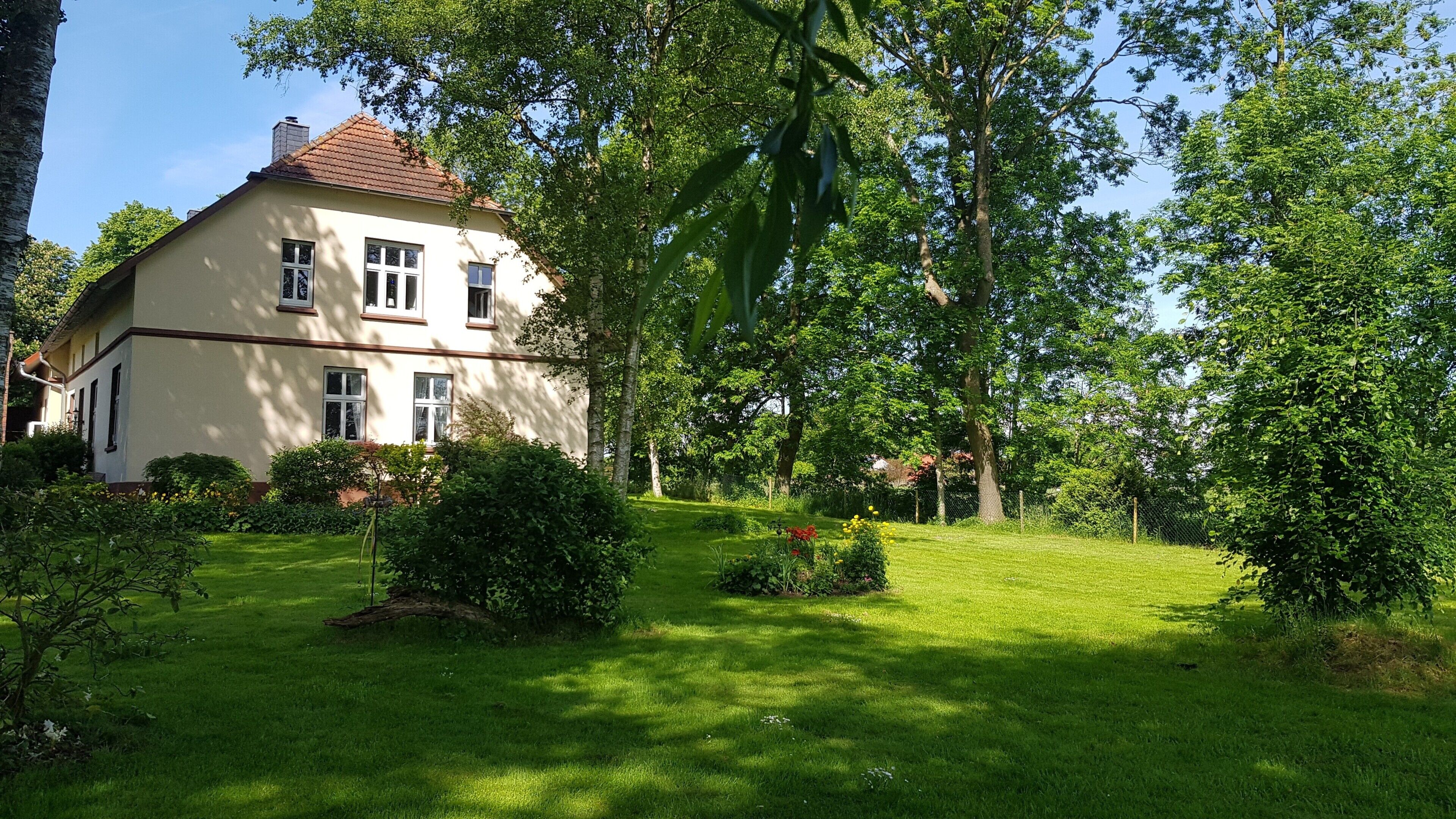 Een huis met twee verdiepingen, een verzorgd gazon en volwassen bomen.