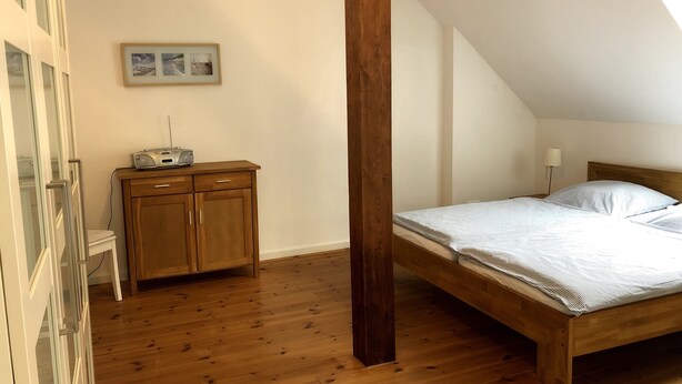 Una camera da letto con un letto di legno, un comodino, una cassettiera e un quadro appeso al muro.